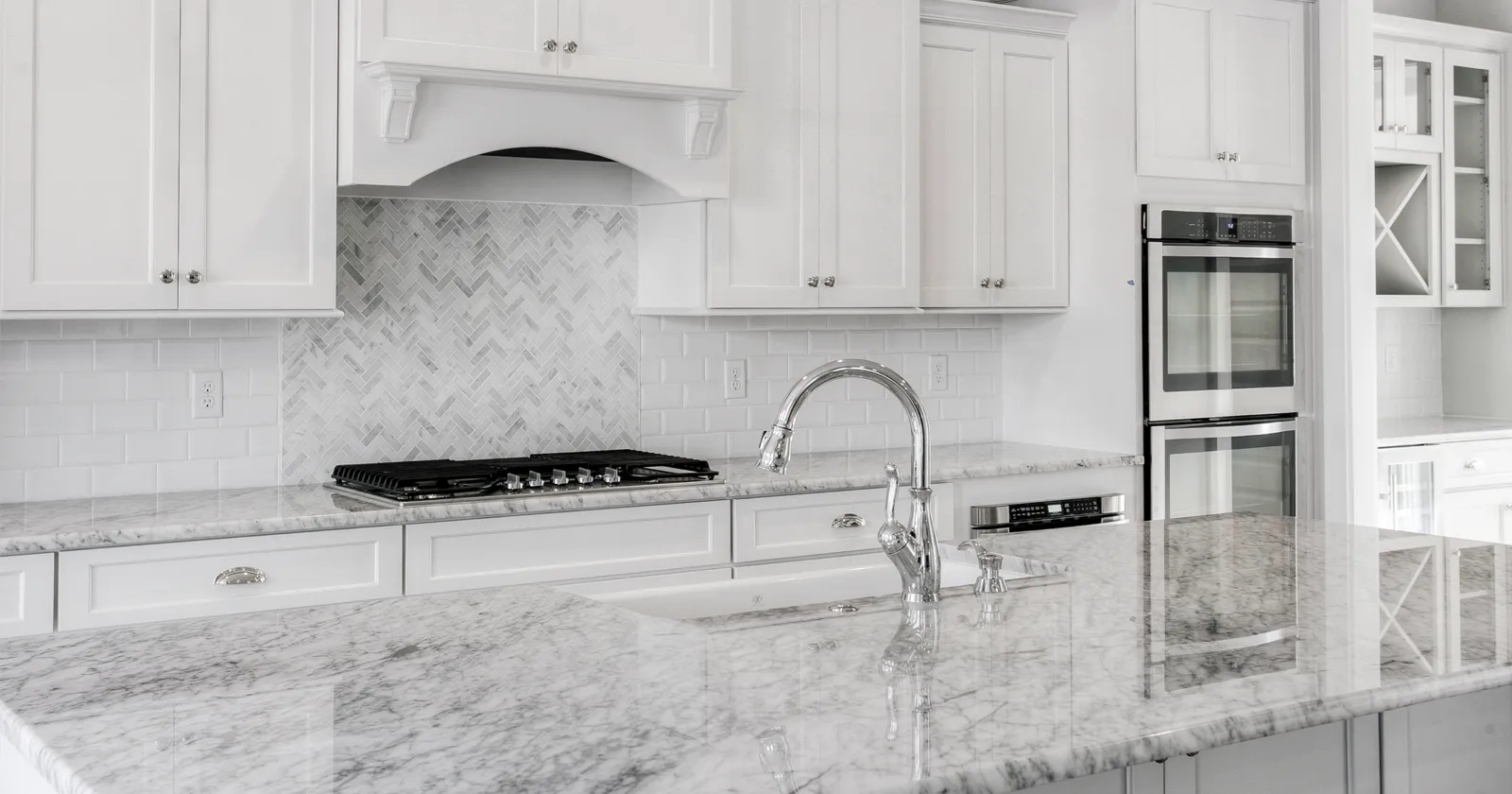 Bright white kitchen with marble countertops, subway tile backsplash, and stainless steel appliances, offering a clean and timeless look.